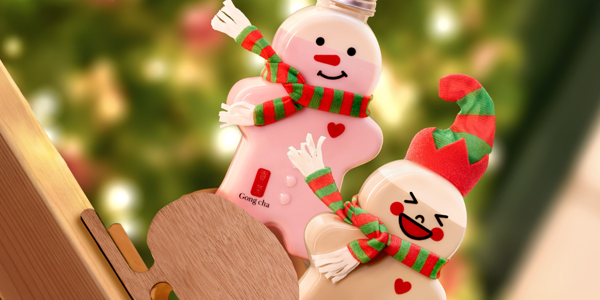 Two festive Gong Cha snowman-shaped drink bottles with red-green scarves, smiling against blurred Christmas lights.