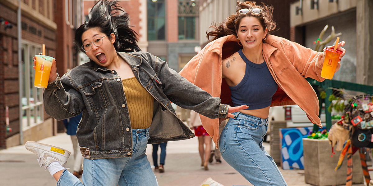 Two joyful young women jump in a city alley, each holding a bright Gong Cha bubble tea cup.