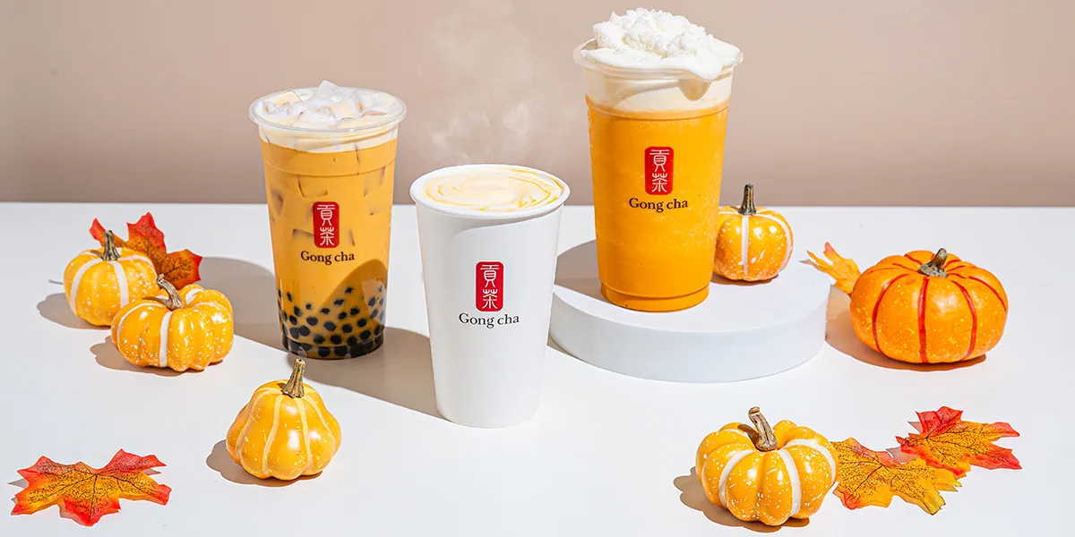 Three Gong Cha drinks—two iced boba and one hot cup—arranged with mini pumpkins and autumn leaves on white.