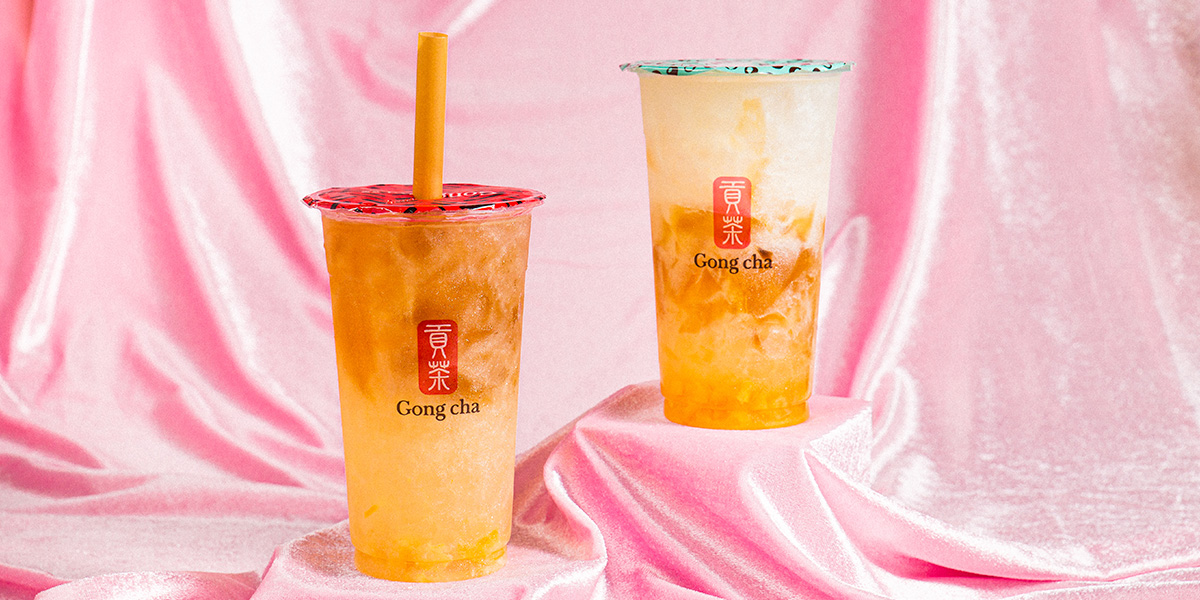 Two Gong Cha bubble tea cups with layered creamy orange and milk tea on a pink satin backdrop.