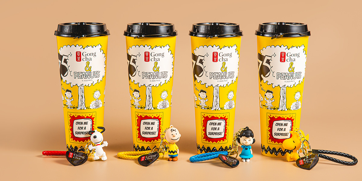 Four Gong Cha yellow limited-edition Peanuts bubble tea cups with Snoopy and Charlie Brown keychain figures on a beige background.