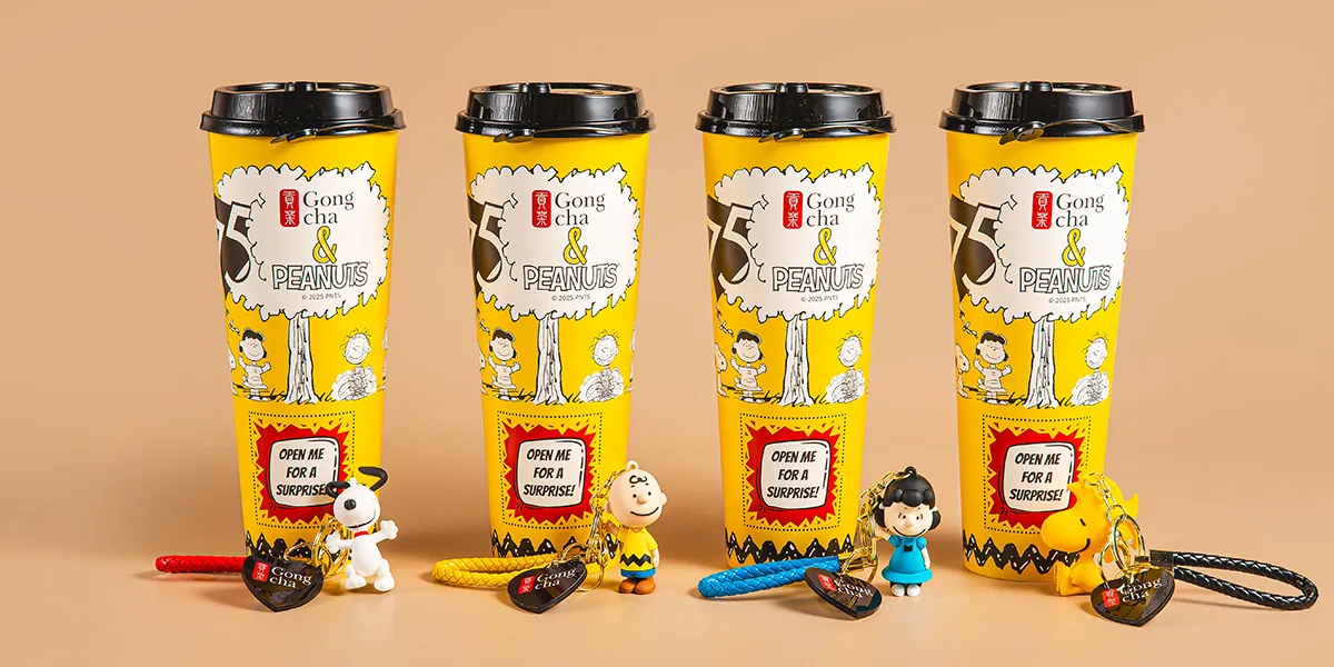 Four Gong Cha yellow limited-edition Peanuts bubble tea cups with Snoopy and Charlie Brown keychain figures on a beige background.