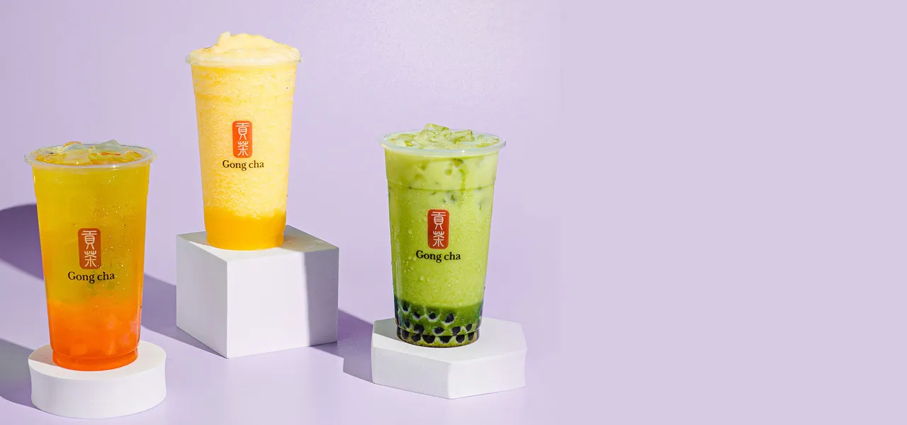 Three Gong Cha bubble tea drinks—icy mango slush, citrus tea, and matcha milk tea with black pearls—on white pedestals against a lavender backdrop
