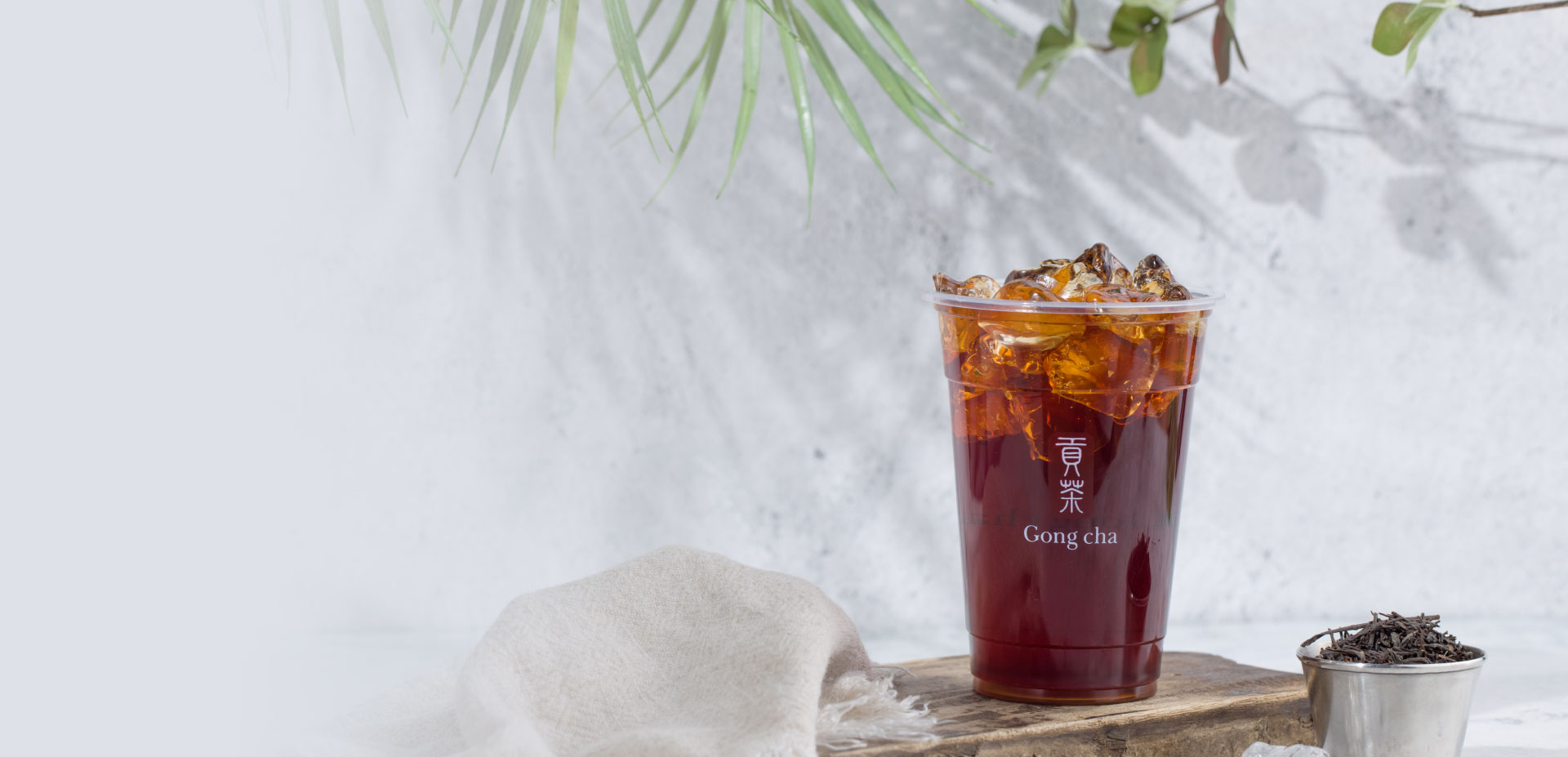 A refreshing iced tea from Gong Cha in a clear cup with ice, set on a wooden board with greenery in the background.