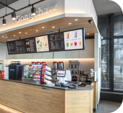 Modern bubble tea shop interior with a wooden counter, digital menu displays, and beverage preparation area. Bright and inviting atmosphere.