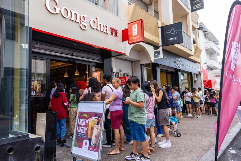 People lined up outside a Gong Cha store on a busy street, waiting to enter. A sign displays promotional offers near the entrance.