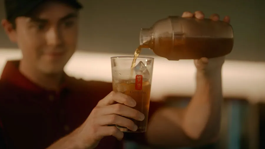 A person pours iced tea from a pitcher into a glass filled with ice cubes.