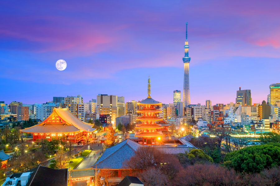 Tokyo skyline at dusk with Tokyo Skytree, illuminated pagoda, and cityscape under a vibrant sky and full moon.
