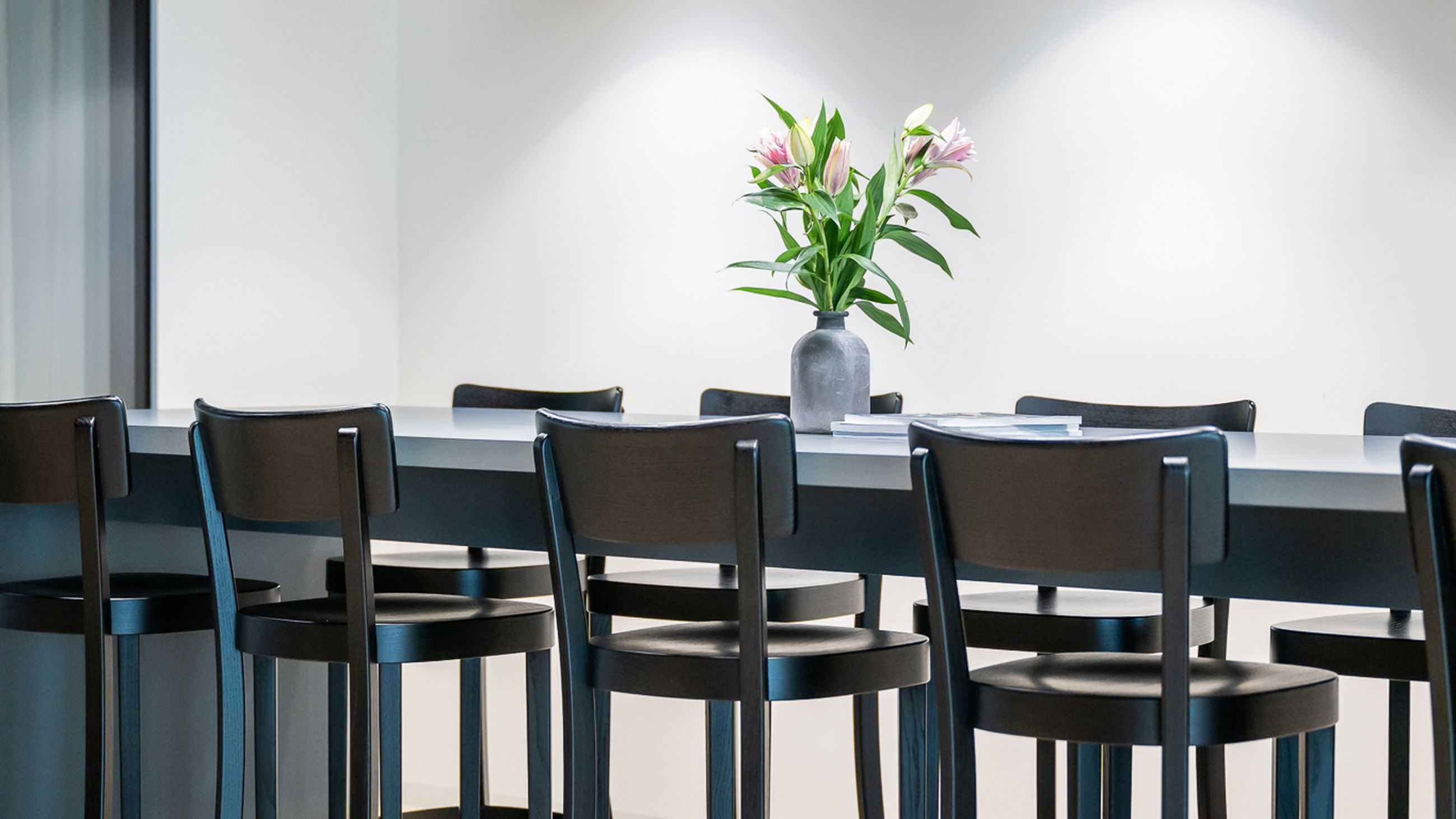 Eleganter Meetingbereich mit hohem Tisch, schwarzen Barstühlen und modernen Pendelleuchten unter dunkler Decke.