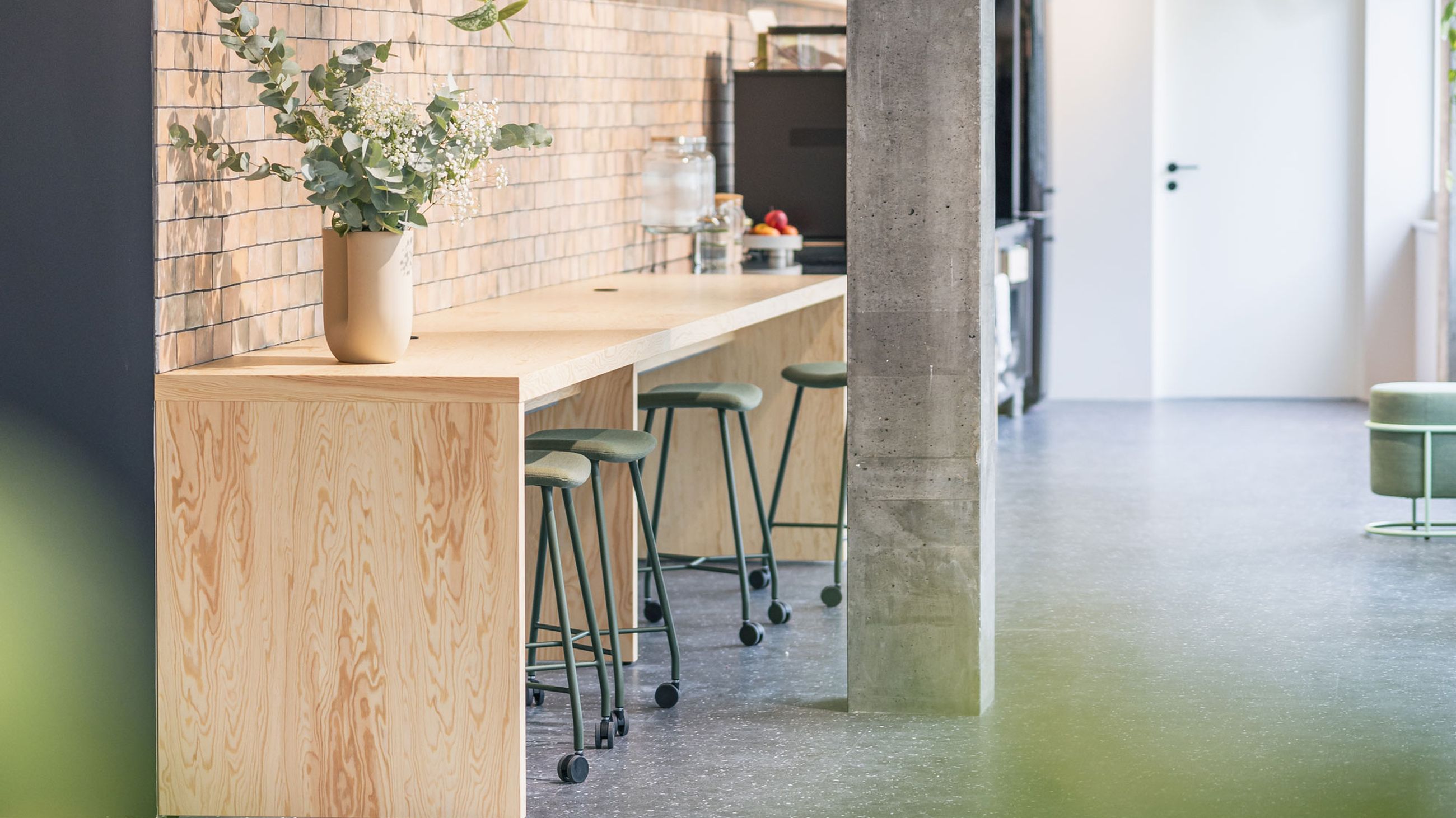 Stilvoller Bürobereich mit hoher Bartheke, Backsteinwand, Pflanzen und industriellen Designelementen.