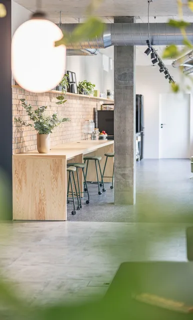 Stilvoller Bürobereich mit hoher Bartheke, Backsteinwand, Pflanzen und industriellen Designelementen.