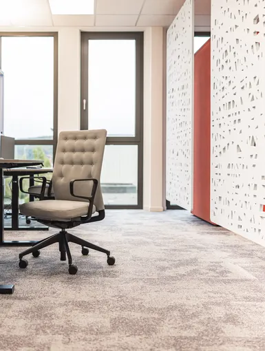 Höhenverstellbare Tische, graue Teppichwelt, weiße Akustiktrenner und auffällige rote Telefonbox.