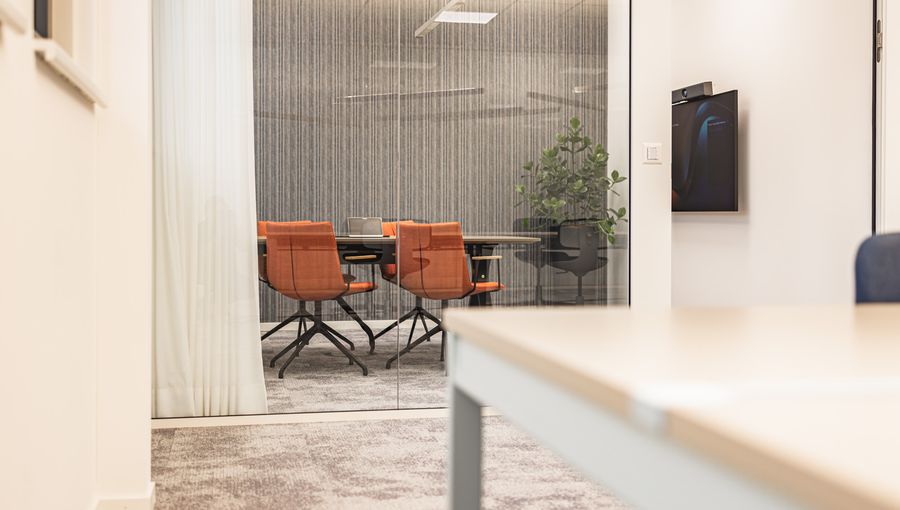 Kompakter Besprechungsraum mit orangenen Stühlen und strukturierter Akustikwand. Ruhig, reduziert.