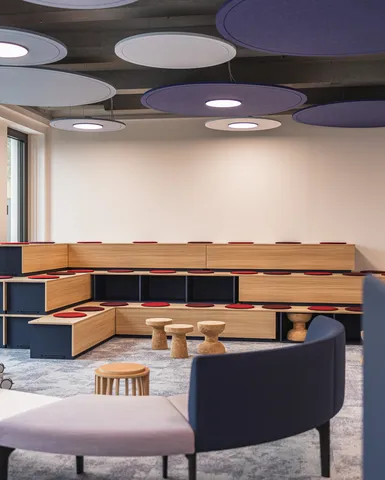 Modulare Holztribüne mit roten Sitzpads. Offener Raum für Workshops und Präsentationen, akustische Deckenelemente.