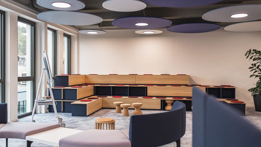 Modulare Holztribüne mit roten Sitzpads. Offener Raum für Workshops und Präsentationen, akustische Deckenelemente.