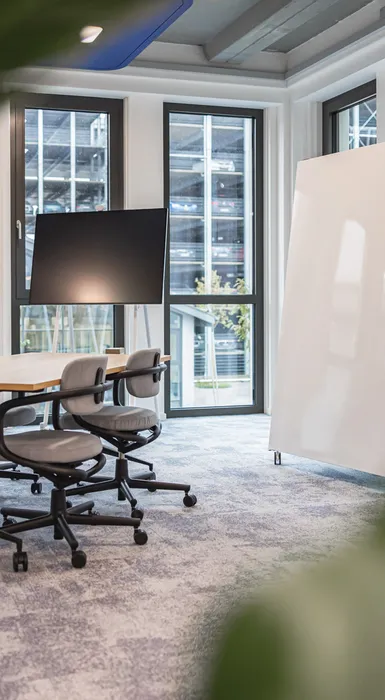 Heller Kreativraum mit mobilen Whiteboards, großem Tisch und flexiblen Drehstühlen. Viel Tageslicht, klare Linien.