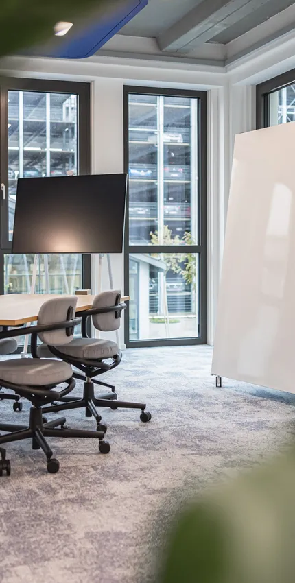 Heller Kreativraum mit mobilen Whiteboards, großem Tisch und flexiblen Drehstühlen. Viel Tageslicht, klare Linien.