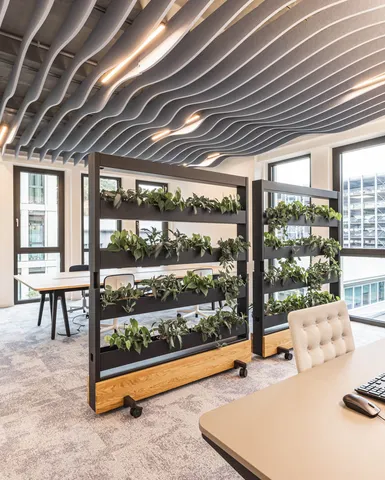 Zeitgemäßer Büroarbeitsplatz mit vertikalen Pflanzenregalen und wellenförmigen Akustikelementen an der Decke.