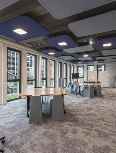 Heller und offener Arbeitsbereich mit großen Fensterfronten, modularen Tischen und akustischen Deckenpaneelen.