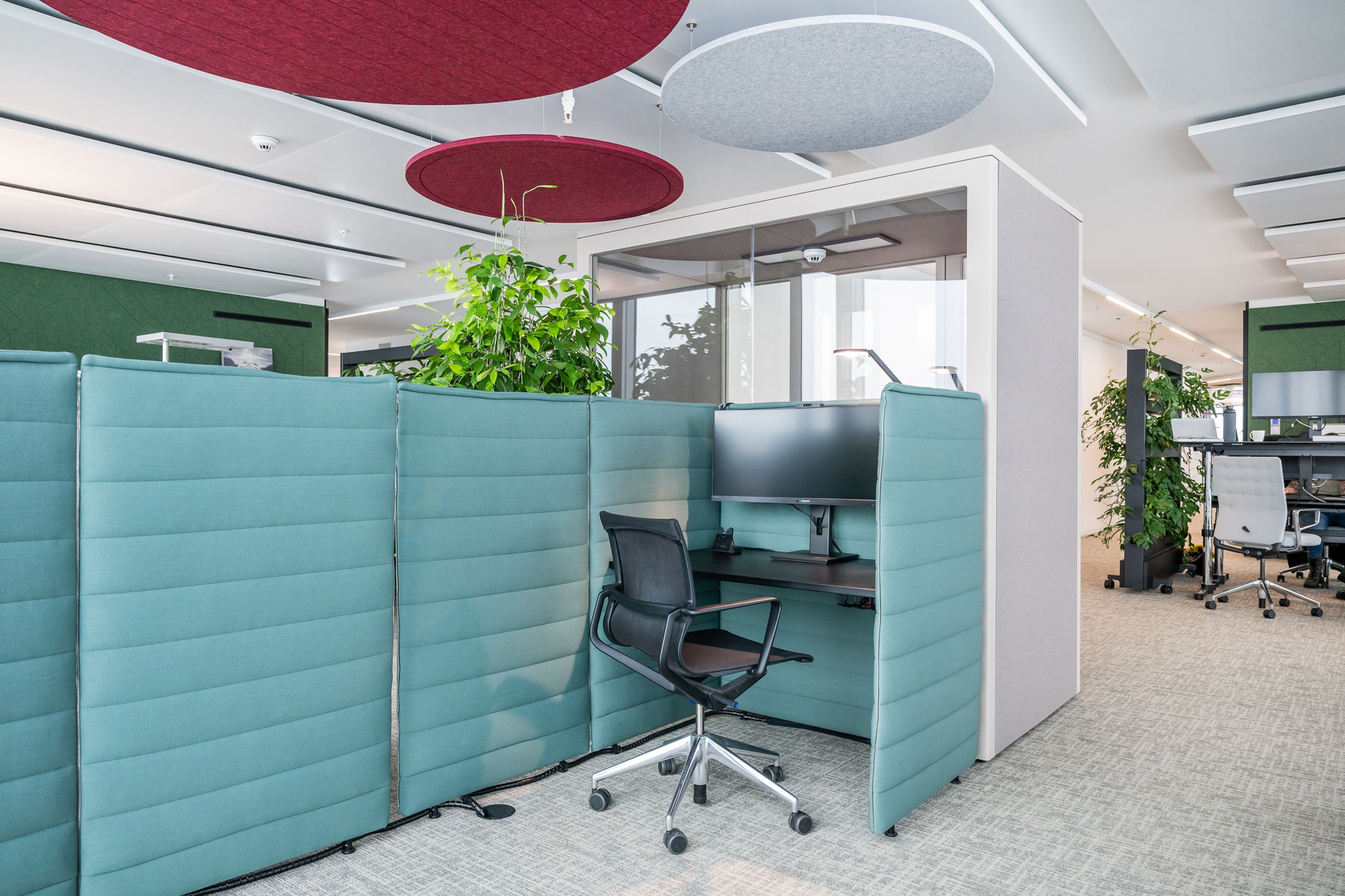 Arbeitsbereich mit hohem Tisch, Barhockern und Laptop unter roten Akustiksegeln in hellem Open Workspace.