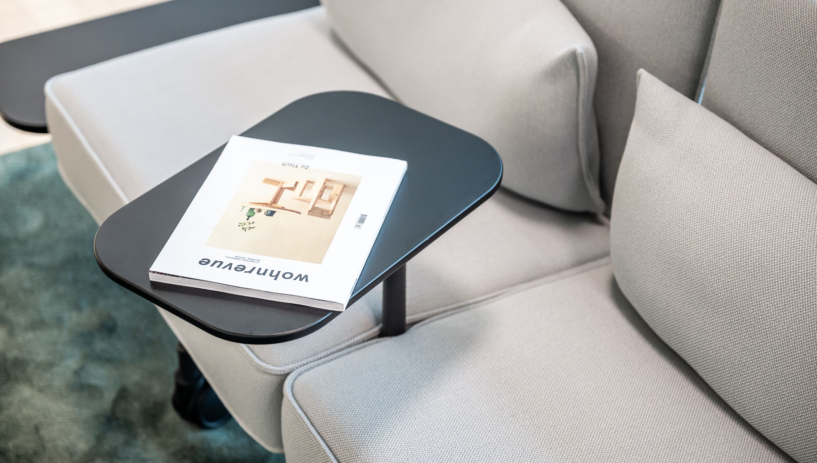 Detailaufnahme eines hellgrauen Sofas mit integriertem Ablagetisch und aufgelegtem Wohnen-Magazin.
