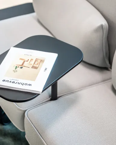 Detailaufnahme eines hellgrauen Sofas mit integriertem Ablagetisch und aufgelegtem Wohnen-Magazin.