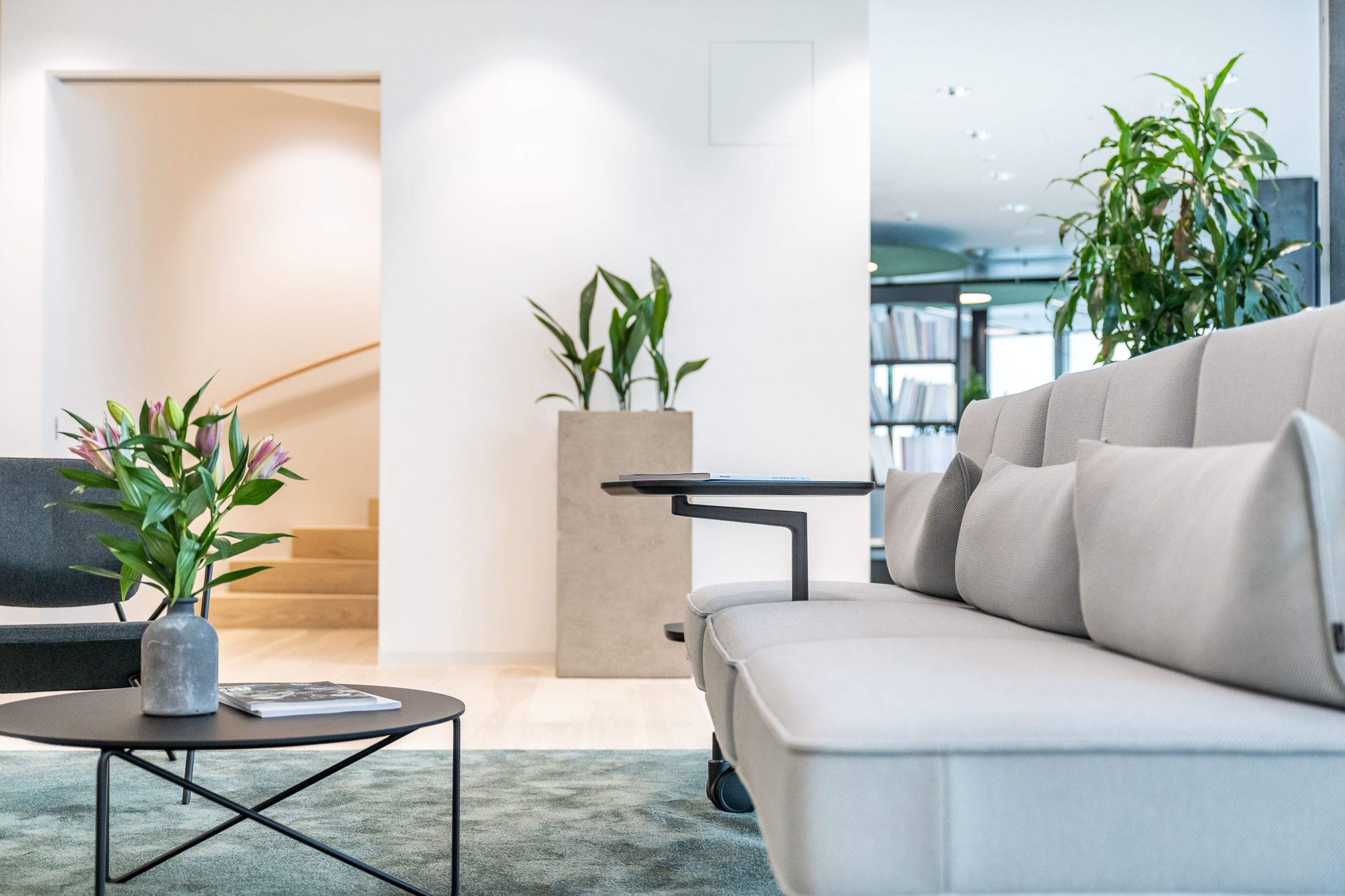 Detailaufnahme eines modernen Lounge-Sofas mit Beistelltisch, Pflanzen und offenem Treppenaufgang im Hintergrund.