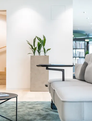 Detailaufnahme eines modernen Lounge-Sofas mit Beistelltisch, Pflanzen und offenem Treppenaufgang im Hintergrund.