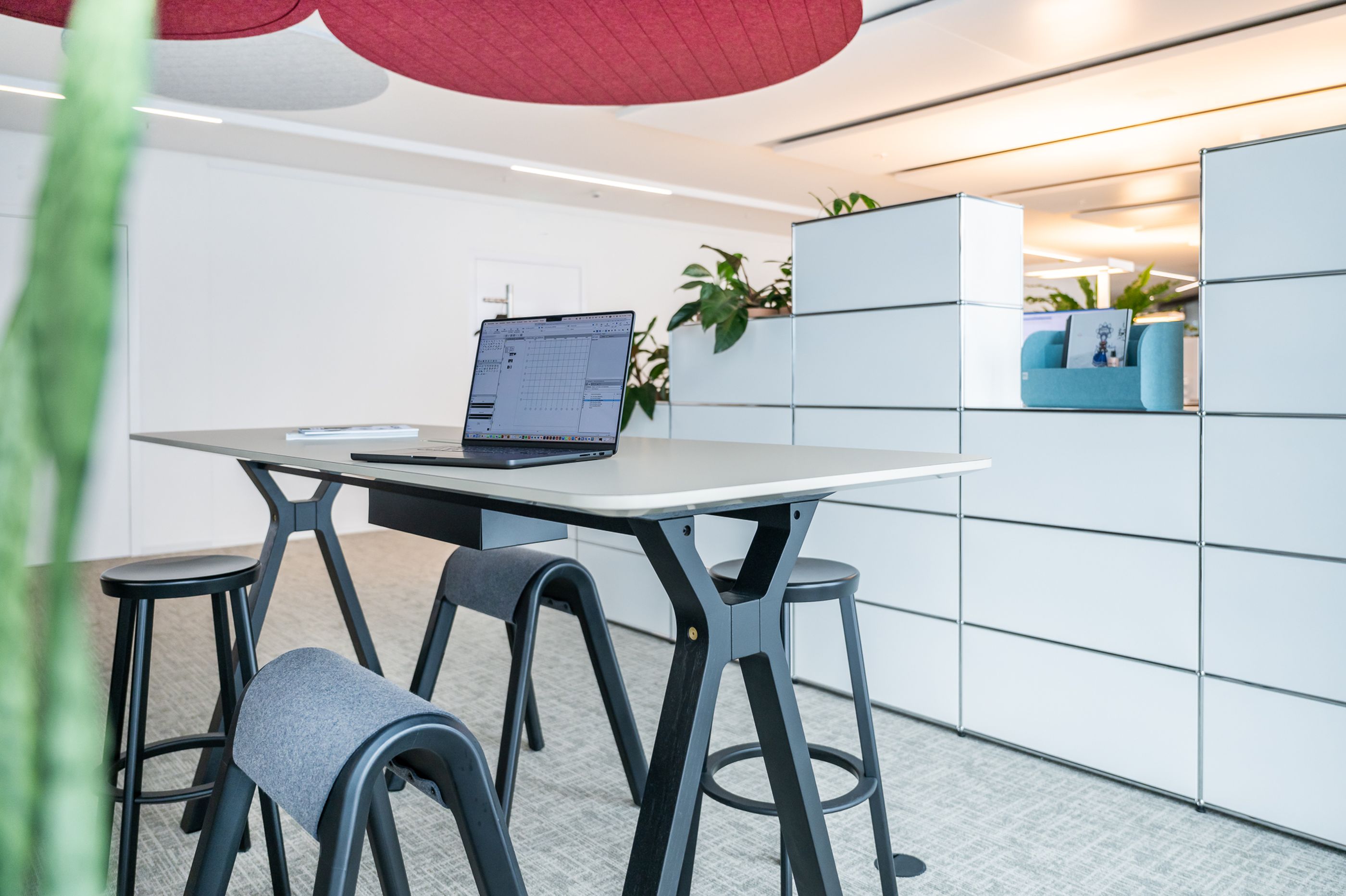 Elegante Büroküche mit schwarzer Küchenzeile, heller Arbeitsplatte und vier schwarzen Barhockern auf Holzboden.