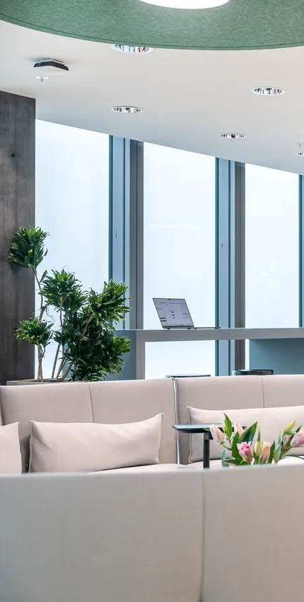 Moderner Loungebereich mit hellen Sofas, großem Bücherregal und hohen Bartischen vor bodentiefen Fenstern.