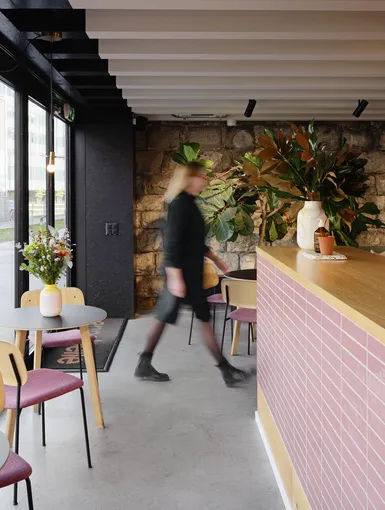 Nahaufnahme eine Theke mit pinken Kacheln. Daneben Coffee-Table mit Stühlen. Eine Person läuft vorbei.