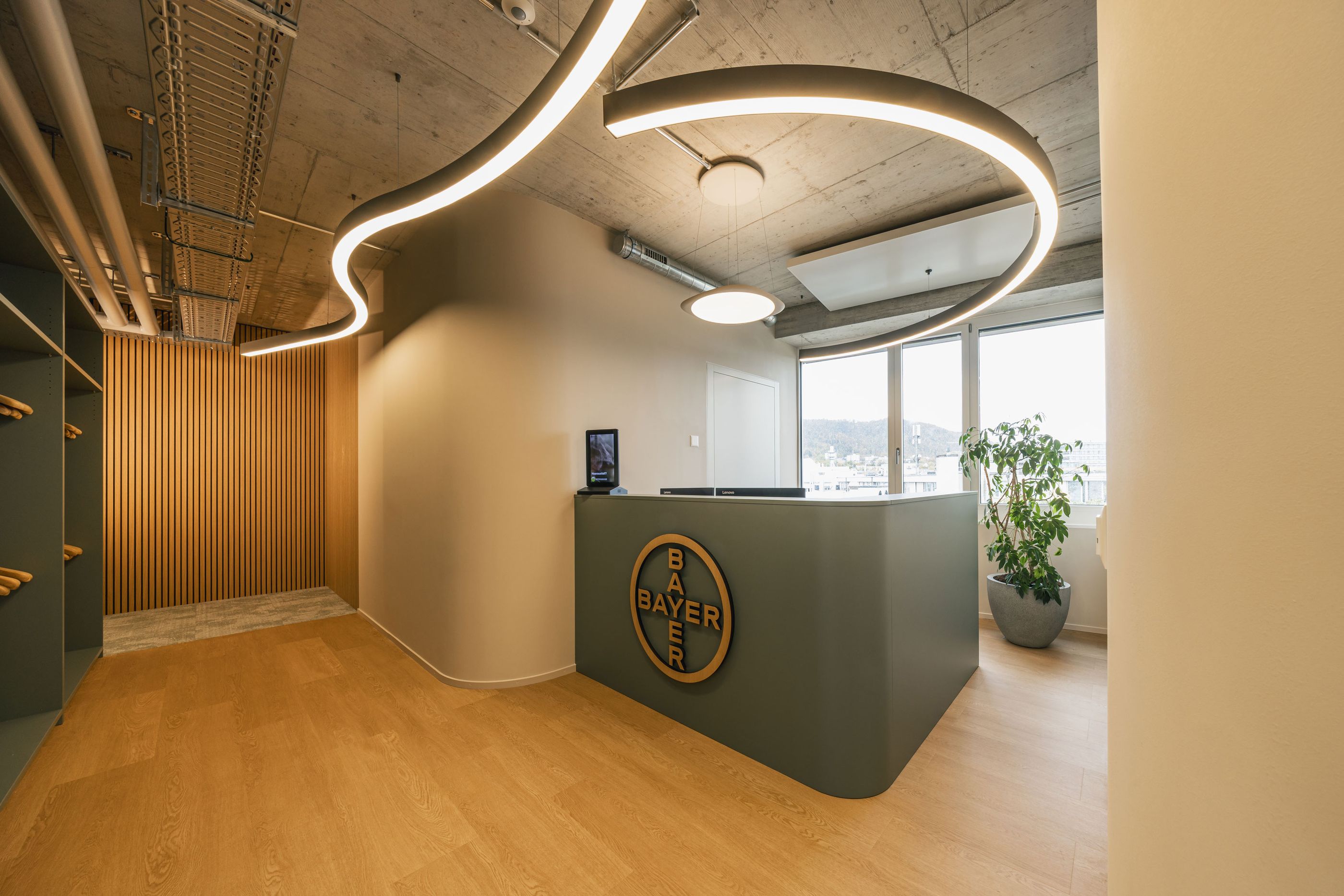 Empfangsbereich mit gebogener LED-Beleuchtung, Holzlamellenwand und großem Bayer-Logo an der Theke.