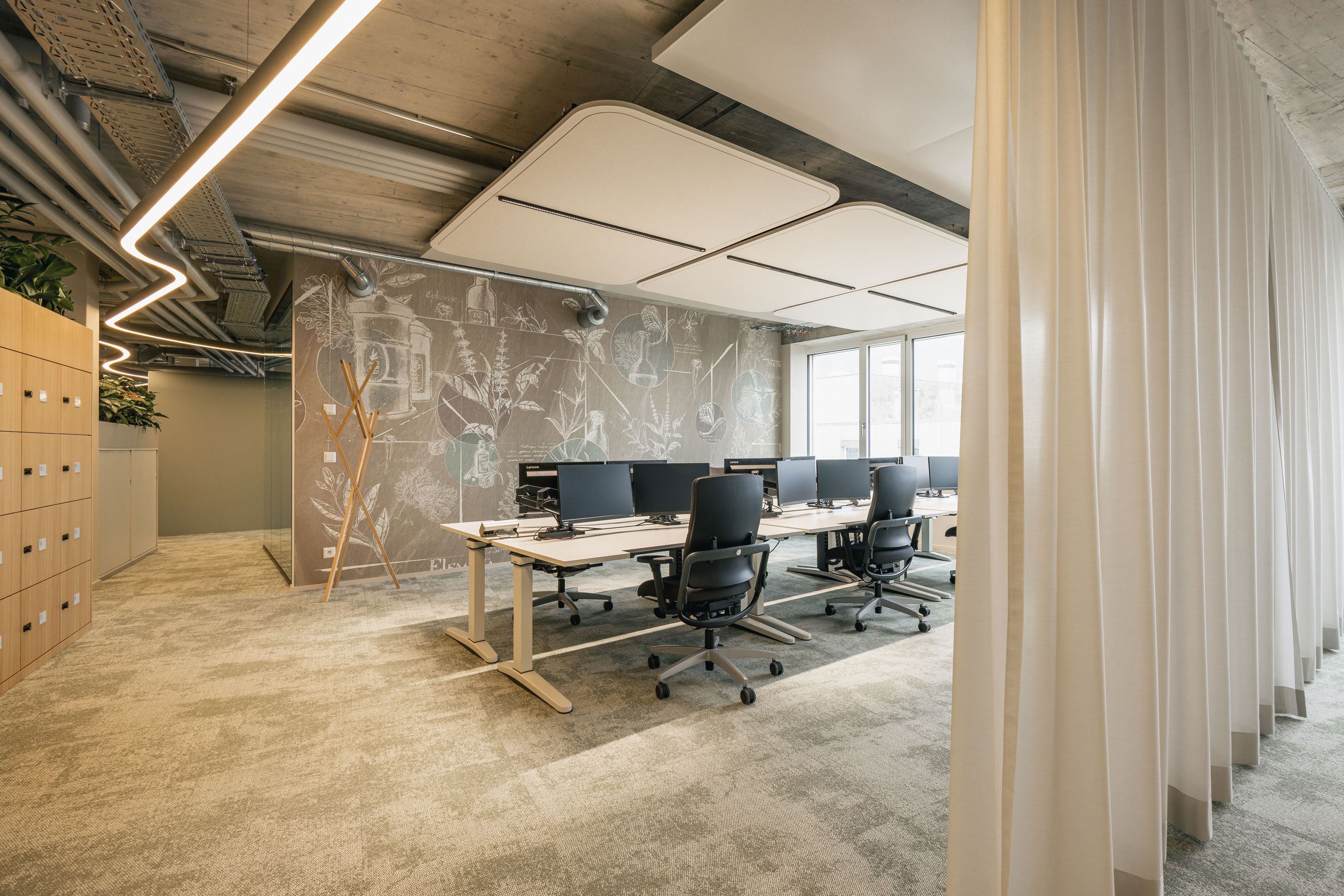 Reihen höhenverstellbarer Arbeitsplätze vor einer großformatigen Wandillustration im botanisch-technischen Stil.