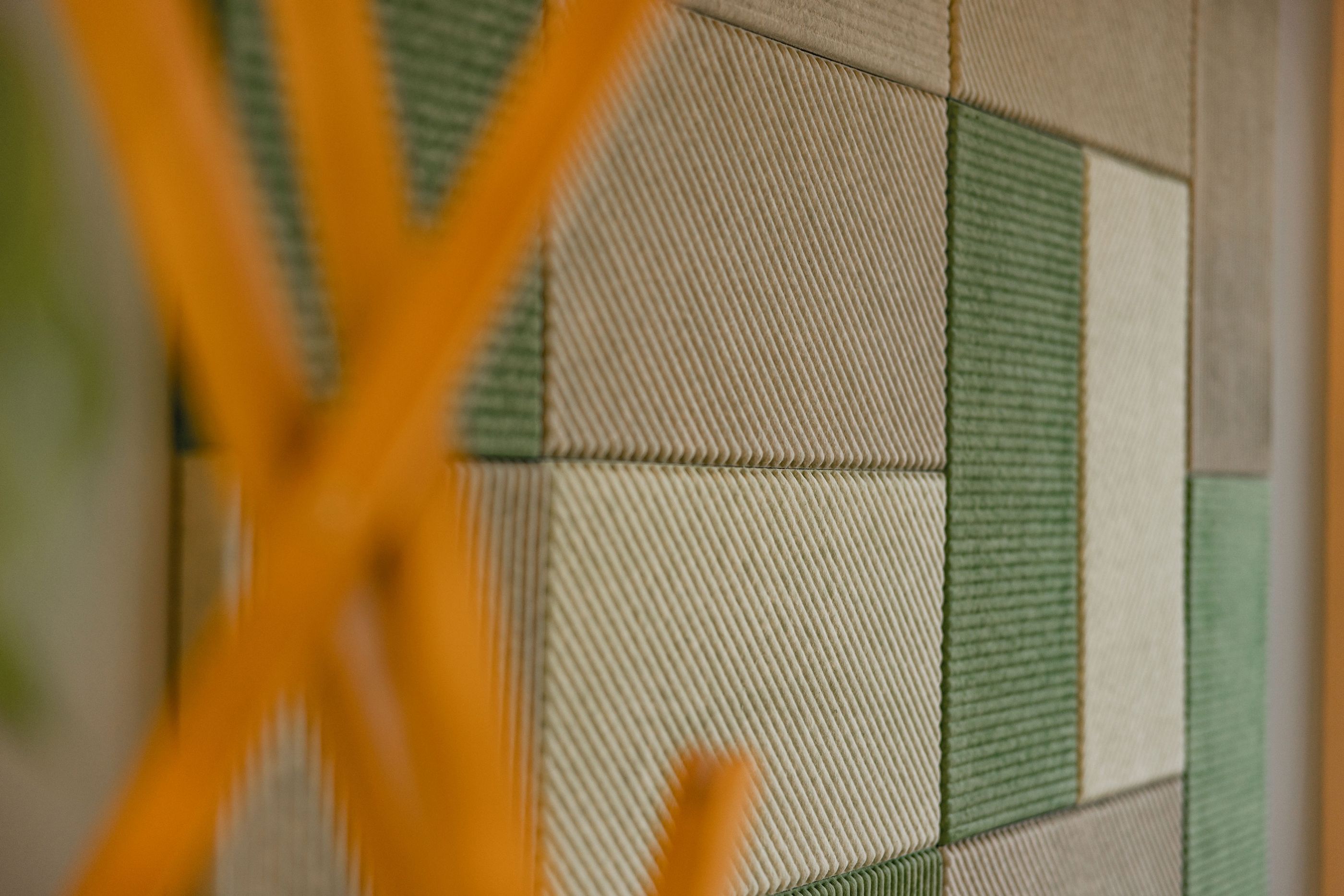Detailaufnahme grüner und beige strukturierter Akustikpaneele an einer Wand.