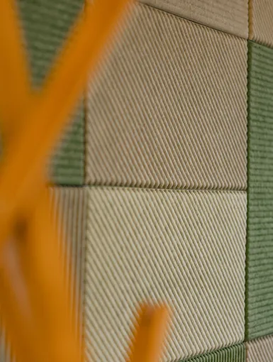 Detailaufnahme grüner und beige strukturierter Akustikpaneele an einer Wand.
