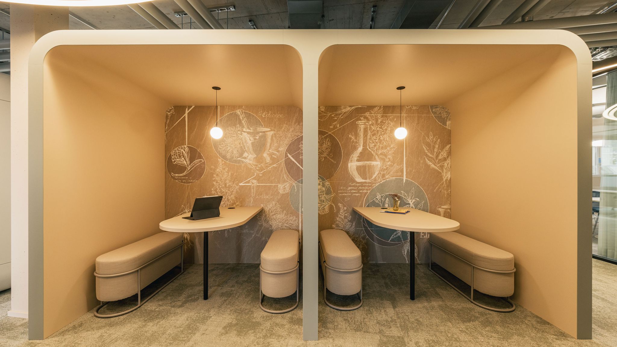 Zwei beige Meeting-Nischen mit Tischen, Sitzbänken und warmen Pendelleuchten vor einer illustrierten Wand.