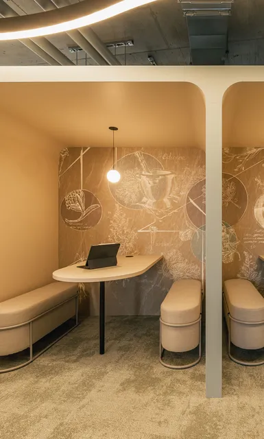 Zwei beige Meeting-Nischen mit Tischen, Sitzbänken und warmen Pendelleuchten vor einer illustrierten Wand.