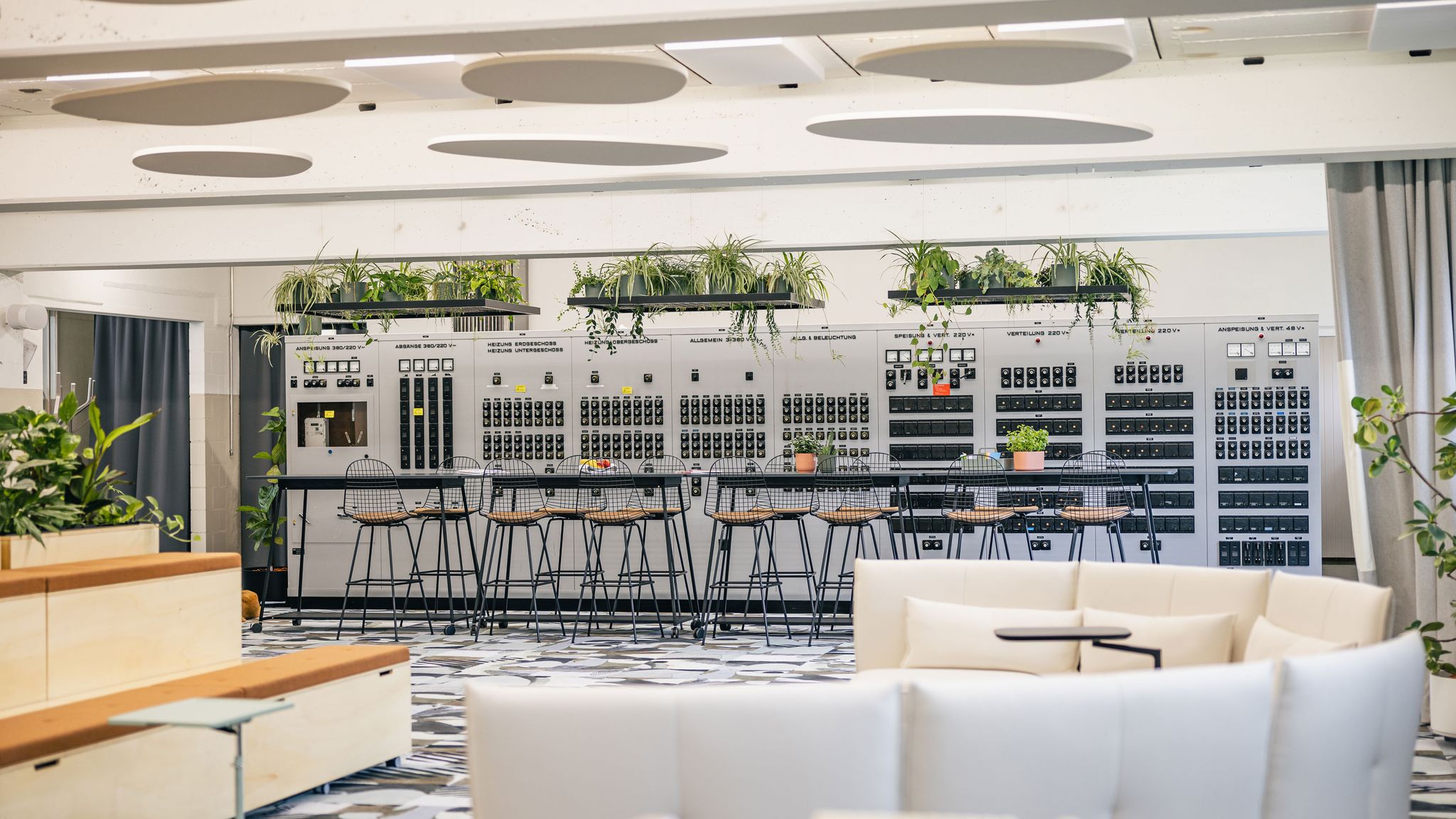 Offener Meetingbereich mit Pflanzen, Holzpodesten und großem Bildschirm.