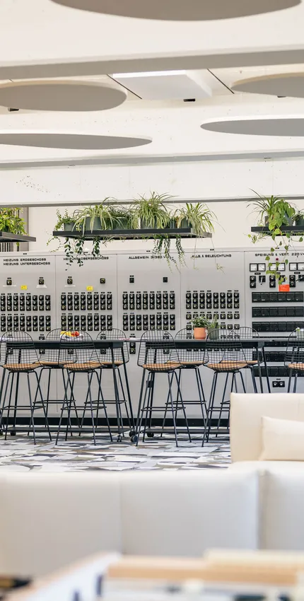 Offener Meetingbereich mit Pflanzen, Holzpodesten und großem Bildschirm.