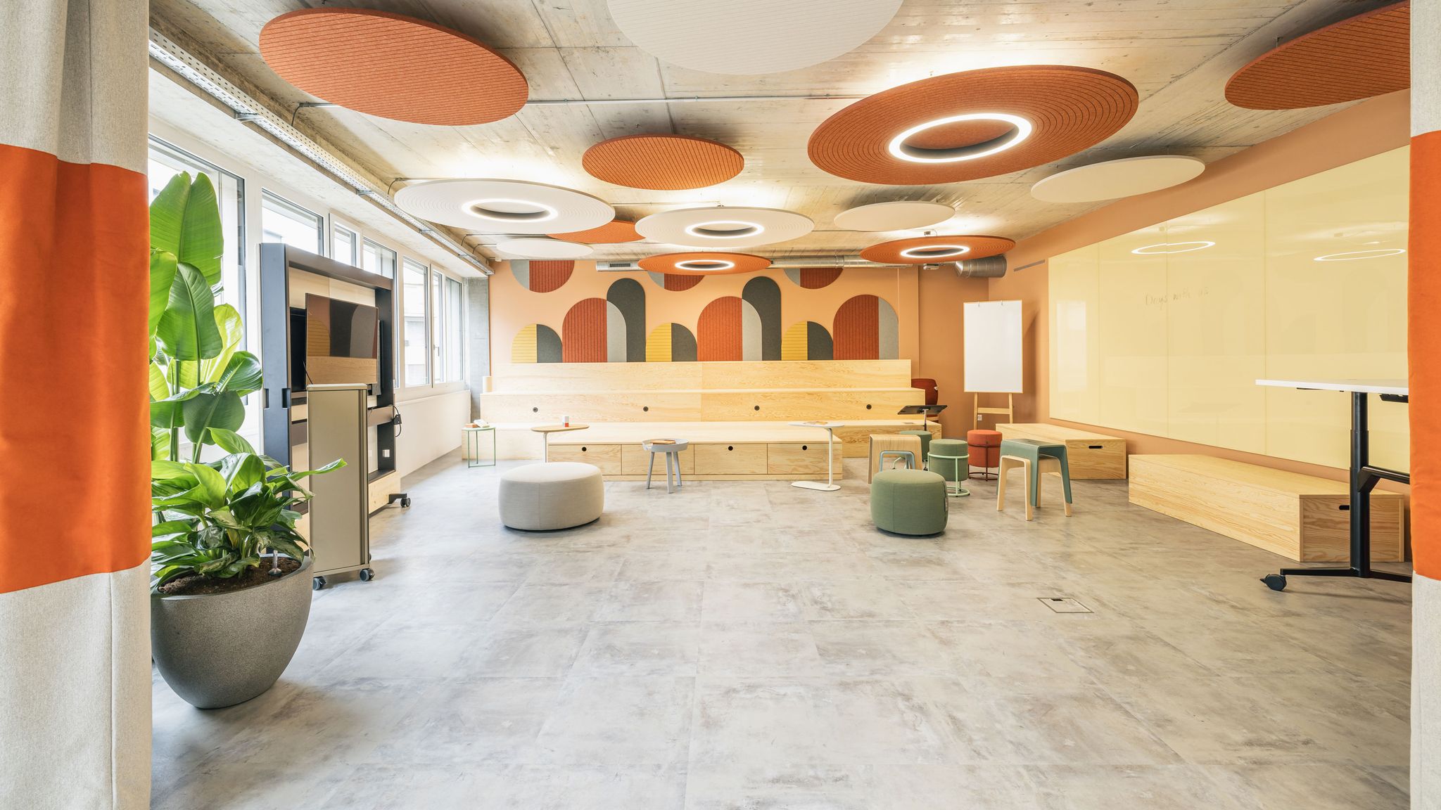 Offener Kreativraum mit großen runden Akustikelementen, heller Holzbühne und flexiblen Workshopmöbeln.