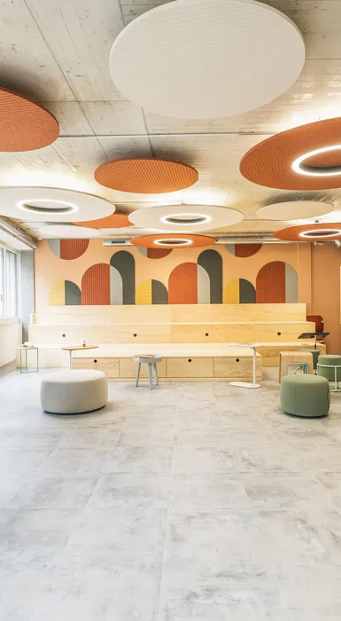 Offener Kreativraum mit großen runden Akustikelementen, heller Holzbühne und flexiblen Workshopmöbeln.