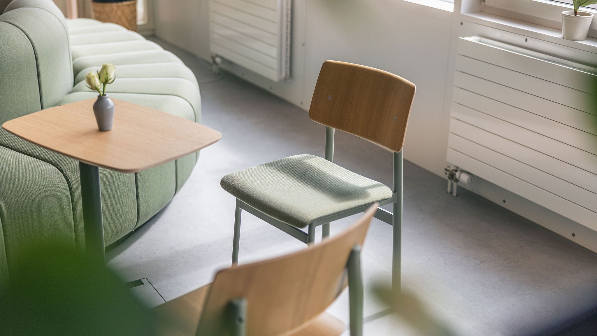 Gemütlicher Büro-Loungebereich mit grünem Sofa, Holzstühlen und kleinen Beistelltischen im Tageslicht.