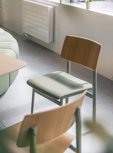 Gemütlicher Büro-Loungebereich mit grünem Sofa, Holzstühlen und kleinen Beistelltischen im Tageslicht.