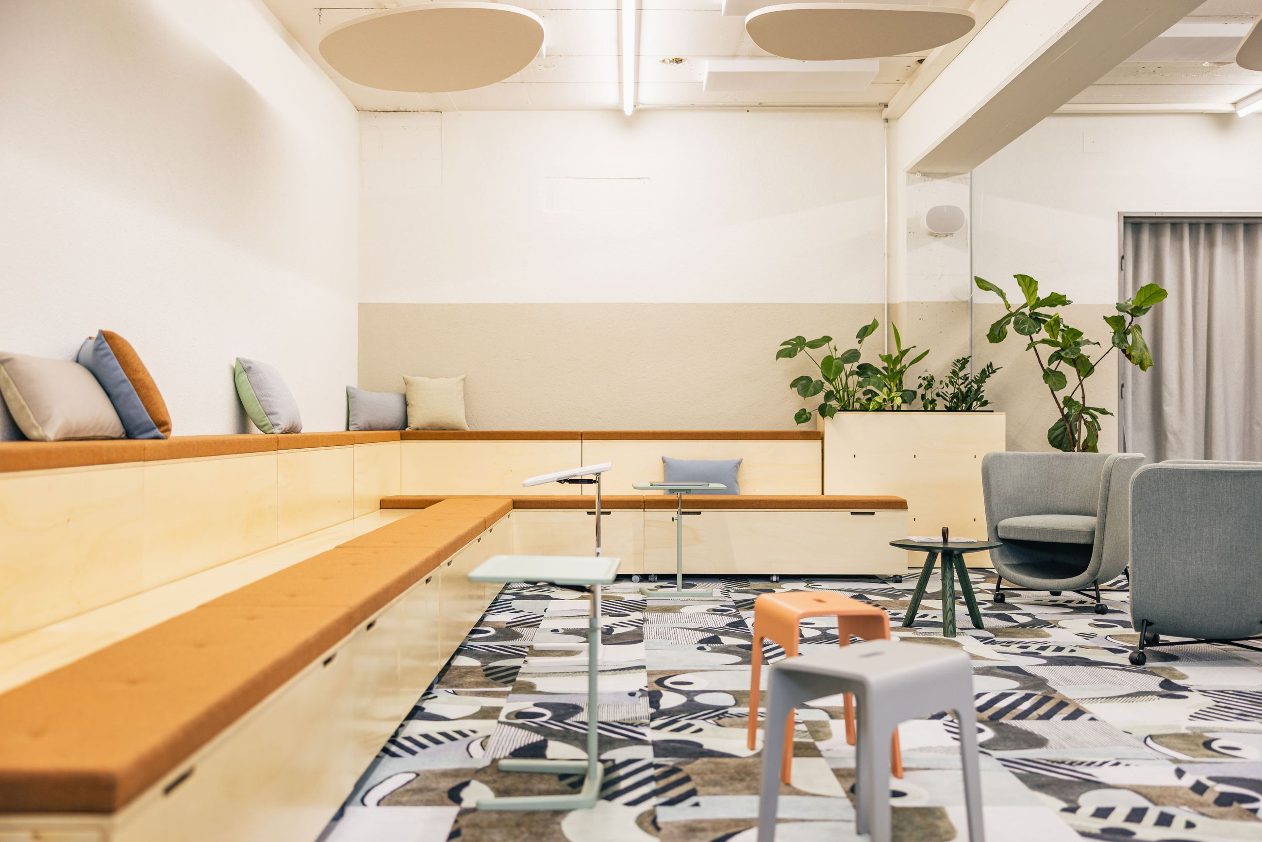 Offener Meetingbereich mit Pflanzen, Holzpodesten und großem Bildschirm.