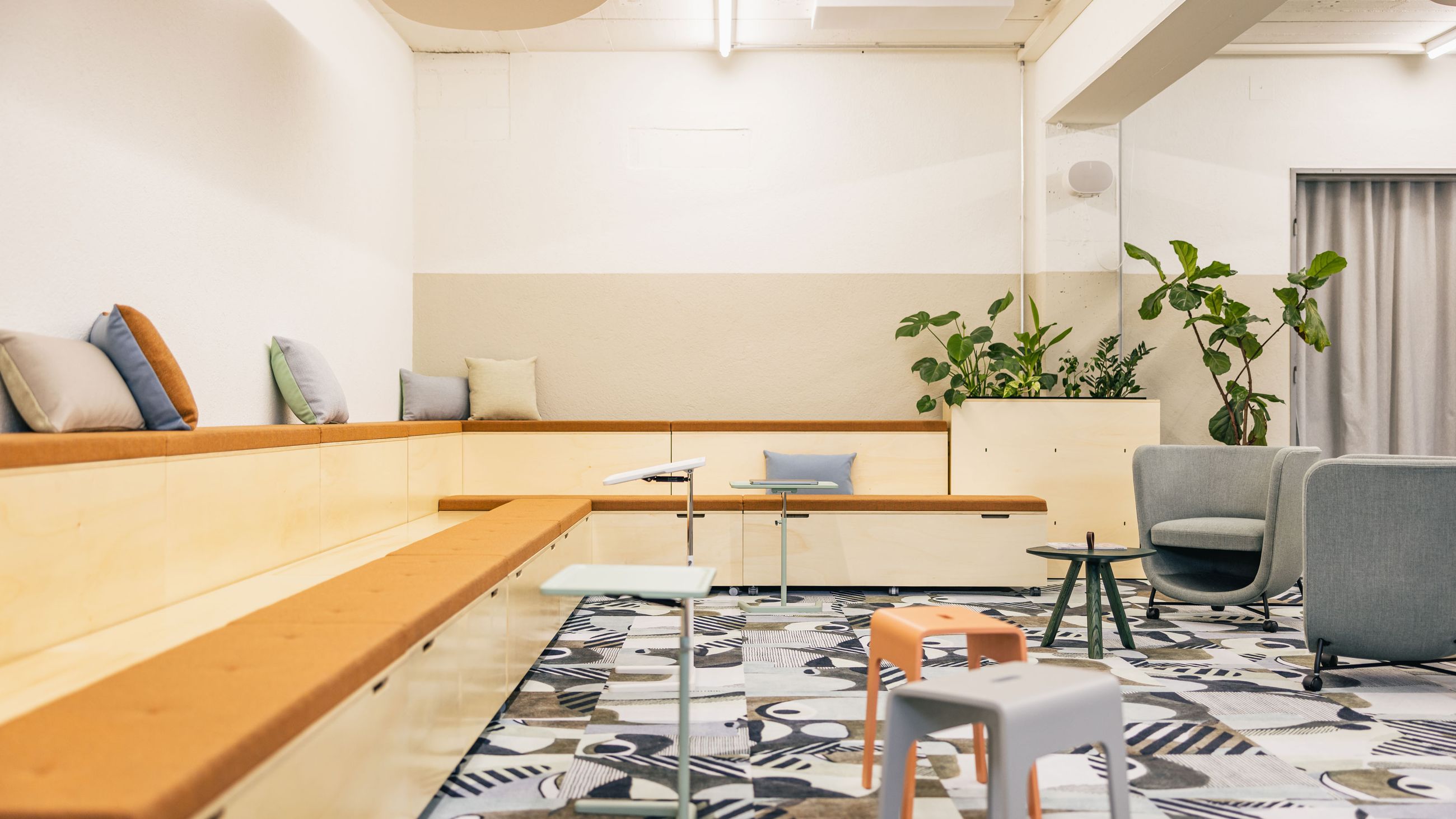 Offener Meetingbereich mit Pflanzen, Holzpodesten und großem Bildschirm.