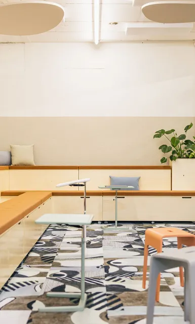 Offener Meetingbereich mit Pflanzen, Holzpodesten und großem Bildschirm.