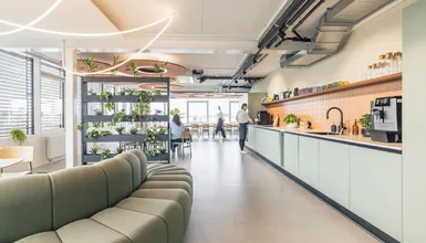 Heller Office-Community-Bereich mit Designsofa, Pflanzenregal und moderner Büroküche.