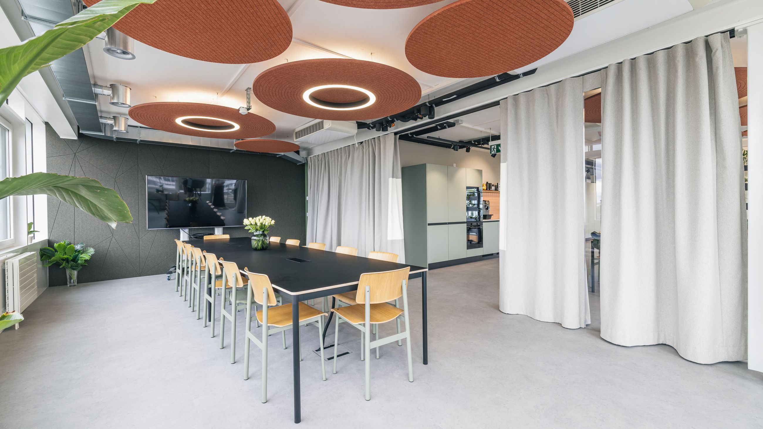 Offener Workshopraum mit langem Besprechungstisch, Akustikdecken und großem Bildschirm.