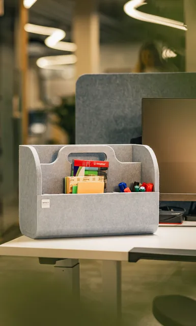 Grauer Büro-Organizer mit Stiften und Notizen auf einem modernen Arbeitsplatz.