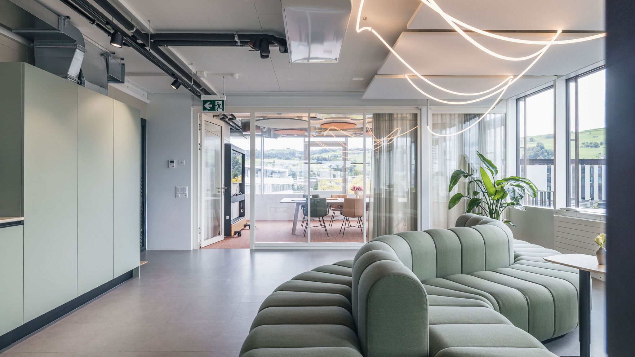 Großer Büro-Loungebereich mit geschwungenem Sofadesign und Panoramafenstern mit Blick auf die Umgebung.
